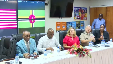 Dominican and U.S. officials seated at a national security meeting, with Dominica and U.S. flags displayed on screens