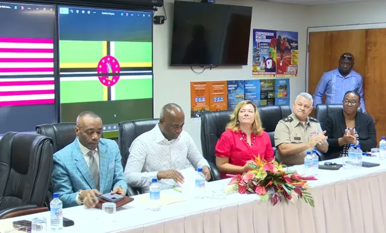 Dominican and U.S. officials seated at a national security meeting, with Dominica and U.S. flags displayed on screens