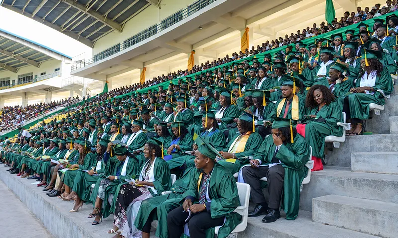 Graduates in green gowns sit in the stands at Windsor Park Sports Stadium during a Dominica State College commencement ceremony.