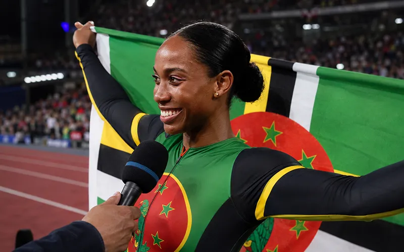 Dominican female track athlete Thea LaFond celebrating in a stadium with the Dominica flag.