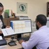 Electoral Office staff and a software contractor review anonymized duplicate confirmation records inside a government office in Dominica, with the Electoral Office logo visible behind them.